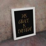 His Grace Is Enough Christian wall art in gold text on a black background, perfect for home decor and inspirational reminders. displayed on the wall in a white frame