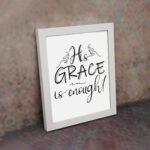 His Grace Is Enough Christian wall art in black cursive font on a white background emphasizing the word 'GRACE'. displayed on the wall in a white frame