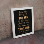 Infidu wall art featuring the text From The Rising of The Sun to The Place Where It Sets, The Name of The Lord is to Be Praised in gold on a black background. displayed on the wall in a white frame