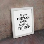 Infidu Christian wall art with Isaiah 54:13 verse in bold black text on a white background, All Your Children Shall Be Taught By The Lord. displayed on the wall in a white frame