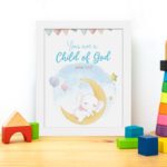 You Are a Child of God wall art featuring a white elephant on a crescent moon with stars and pastel flags. displayed on the table in a white frame