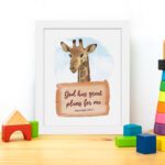 Jeremiah 29:11 Bible verse wall art featuring a cheerful giraffe on a sky-blue background, designed for children's rooms. displayed on the table in a white frame