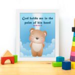 God Holds Me In The Palm Of His Hand Isaiah 49:16 Bible verse wall art for kids featuring a cartoon bear and fluffy clouds. displayed on the table in a white frame