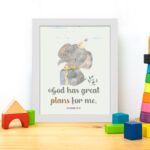 Wall art featuring a grey elephant with a party hat and a yellow gift, displaying the text God Has Great Plans For Me. displayed on the table in a white frame