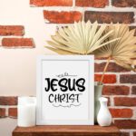 Jesus Christ wall art in black curly font on a white background, showcasing elegant Christian design. displayed on the table in a white frame