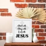 Start With Jesus, Stay With Jesus, End With Jesus Bible Verse Wall Art in Black and White with Light Grey Cross Background displayed on the table in a white frame