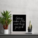 Christian wall art with the quote 'Getting wisdom is the wisest thing you can do' from Proverbs 4:7 in white text on a black background. displayed on the table in a white frame