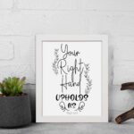 Wall art featuring the quote Your Right Hand Upholds Me from Psalm 63:8 in black text on a white background with floral designs displayed on the wall in a white frame