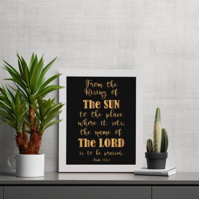 Infidu wall art featuring the text From The Rising of The Sun to The Place Where It Sets, The Name of The Lord is to Be Praised in gold on a black background. displayed on the table in a white frame