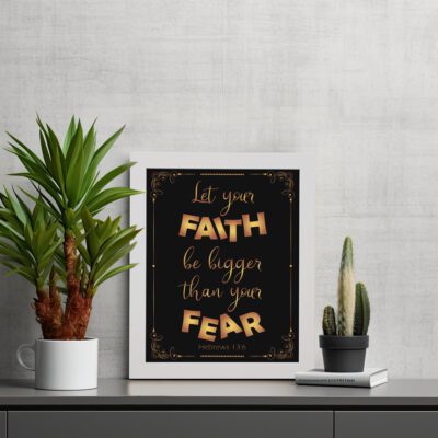 Infidu wall art with the text "Let your faith be bigger than your fear" in gold and bronze, with the Bible verse Hebrews 13:6 on a black background. displayed on the table in a white frame