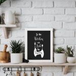 In This Kitchen We Lick The Spoon wall art with white cursive and bold fonts, black background, and stylish cutlery illustrations. displayed on the table