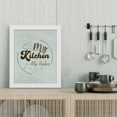 My Kitchen My Rules" kitchen wall art with a light green background, brown text, and a whimsical chef's hat above the words. displayed on the table