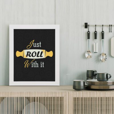 Just Roll With It kitchen wall art with white and yellow text, rolling pin illustration, and faint circular patterns on a black background. displayed on the table