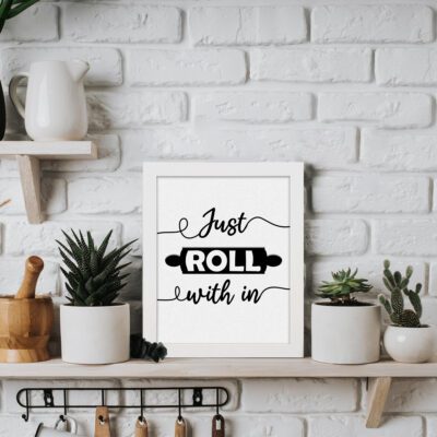 Just Roll With It kitchen wall art with black text and a rolling pin illustration on a white background, offering a clean and bold look. displayed on the table