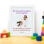 Be Strong and Courageous Joshua 1:9 Bible verse wall art featuring Jesus and two children with a soft blue background. displayed on the table in a white frame