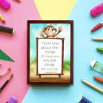 Wall art featuring a happy monkey holding a sign with the verse 'Think only about the things in heaven' from Colossians 3:2. displayed on the wall in a brown frame in a colorful background