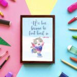 Wall art featuring a joyful bear in winter clothes holding a heart, with the verse We love because He first loved us from 1 John 4:19. displayed on the wall in a brown frame with a colorful background