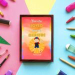 Colorful wall art featuring a happy child holding a heart with the quote You Are Loved Beyond Measure and Romans 8:38. displayed on the wall in a brown frame in a colorful background