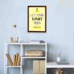 Infidu wall art featuring a lightbulb and the verse Let Your Light Shine from Matthew 5:16 in colorful fonts on a yellow background. displayed on the wall in a brown frame