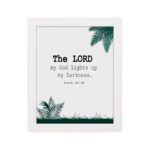 The Lord My God Lights Up My Darkness Psalm 18:28 Bible Verse Wall Art with black text and green tropical leaves on a white background. Wall Art hung on the wall in a white frame