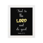 Psalm 37:3 Bible verse wall art with a black background, Lord highlighted in yellow. Christian home decor by Infidu. Wall Art hung on the wall in a white frame