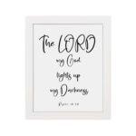 The Lord My God Lights Up My Darkness Psalm 18:28 white text on a black background with a black frame Christian wall art. hung on the wall in a white frame