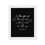 Black wall art with white text and small flower designs quoting When you go through deep waters I will be with you from Isaiah 43:2. hung on the wall in a white frame