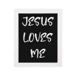 Jesus Loves Me Bible wall art with bold gold text and a decorative gold border on a black background. Wall Art hung on the wall in a white frame