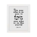 White wall art with black text reading The one who is in you is greater than the one who is in the world 1 John 4:4. hung on the wall in a white frame