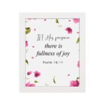 Psalm 16:11 wall art with a white background and pink flower petals, featuring the text 'In His presence there is fullness of joy. Wall Art hung on the wall in a white frame