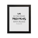 Christian wall art with black text on a white background reading She is far more precious than jewels from Proverbs 31:10 in two font styles. hung on the wall in a black frame