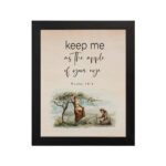 Psalm 17:8 wall art with a soft cursive font and a peaceful illustration of a person sitting under a tree. Wall Art hung on the wall in black frame