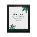 The Lord My God Lights Up My Darkness Psalm 18:28 Bible Verse Wall Art with black text and green tropical leaves on a white background. Wall Art hung on the wall in a black frame