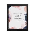 Trust In The Lord And Do Good Psalm 37:3 Bible Verse Wall Art with watercolor and floral designs on a white background. Wall Art hung on the wall in a black frame