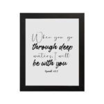 White wall art with black text in script and bold fonts quoting When you go through deep waters, I will be with you from Isaiah 43:2. hung on the wall in a black frame