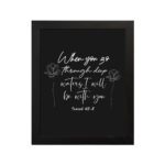 Black wall art with white text and small flower designs quoting When you go through deep waters I will be with you from Isaiah 43:2. hung on the wall in a black frame