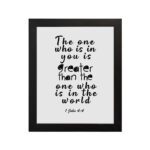 White wall art with black text reading The one who is in you is greater than the one who is in the world 1 John 4:4. hung on the wall in a black frame