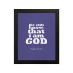 Be Still and Know That I Am God Psalm 46:10 Christian Wall Art with bold white text on a dark purple background. Wall Art hung on the wall in a black frame