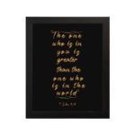 1 John 4:4 Bible verse wall art in gold text on a black background, featuring the quote "The one who is in you is greater than the one who is in the world. hung on the wall in a black frame