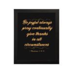 Bible verse wall art featuring 1 Thessalonians 5:16-18 in gold cursive text on a solid black background, arranged in a stacked format. hung on the wall in a black frame