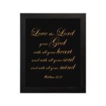 Matthew 22:37 Bible wall art with gold text on a black background, framed in black, reading Love the Lord your God. hung on the wall in a black frame