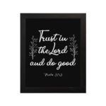 Trust In The Lord And Do Good Psalm 37:3 white text with decorative branches on black background Christian wall art hung on the wall in black frame