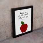 Keep Me As The Apple Of Your Eye" Psalm 17:8 Bible Wall Art featuring a red apple and white background. Perfect Christian home decor. Wall Art displayed on the wall in black frame