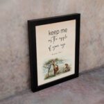 Psalm 17:8 wall art with a soft cursive font and a peaceful illustration of a person sitting under a tree. Wall art is displayed on the wall in a black frame.