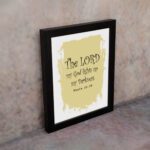 The Lord My God Lights Up My Darkness Psalm 18:28 Bible Verse Wall Art with decorative text on a light yellow paint stroke background. Wall Art displayed on the wall in a black frame