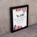 The Lord My God Lights Up My Darkness Psalm 18:28 Bible Verse Wall Art with black text and bold red, orange, blue, and yellow brush strokes on a white background. Wall Art displayed on the wall in a black frame