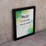 Trust in the Lord and Do Good Psalm 37:3 Bible Verse Wall Art with watercolor green and yellow background. Wall Art displayed on the wall in a black frame