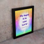 Infidu My Hope Is In You Lord Psalm 39:7 Bible Wall Art with bright blue and pink text and colorful watercolor background Wall Art displayed on the wall in a black frame