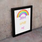 Infidu Jesus Loves Me Bible Wall Art with rainbow arc and colorful text in purple, yellow, and pink fonts Wall Art displayed on the wall in a white frame