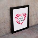 Infidu I Am A Child Of God Bible Wall Art with pink hearts and mixed cursive and print text on a light pink background Wall Art displayed on the wall in a black frame